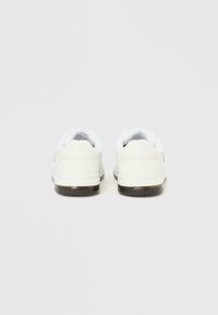 Λευκά αθλητικά παπούτσια με λείο επάνω μέρος, επενδεδυμένο γιακά και υφή σε σκούρα καουτσούκ εξωτερική σόλα. Μινιμαλιστικός σχεδιασμός χωρίς ορατή σήμανση.
