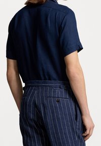 Short-sleeve navy shirt made of linen, featuring a collar and a straight back. Paired with blue pinstriped trousers with pockets.