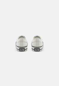 Weiße Canvas-Low-Top-Sneaker mit schwarzen Akzenten und klassischem Logo an der Ferse. Verfügt über eine Gummisohle und ein strukturiertes Obermaterial.