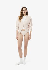 Cardigan rosa chiaro con bottoni frontali e maniche a tre quarti, abbinato a una t-shirt bianca a girocollo e mutandine con pizzo, completato da calzini bianchi.