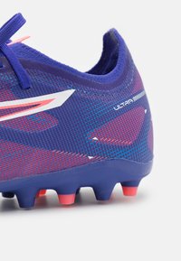 Scarpa da calcio viola e rossa con tomaia in mesh testurizzato, accenti bianchi e numerosi tacchetti in rosa e nero sulla suola.