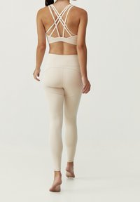 Soutien-gorge de sport beige avec un design de bretelles croisées, associé à un legging taille haute assorti. Texture lisse et silhouette ajustée.