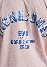 Lyserosa bomull T-skjorte med fet blå grafisk tekst. Designet inkluderer "CK&JONES," "EDTN," og "NORDIC ACTIVE CREW."