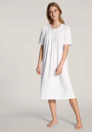 Camicia da notte bianca in cotone con maniche corte, scollatura rotonda e dettagli arricciati sotto il seno, che scende sotto il ginocchio. Tessuto a trama semplice.