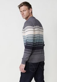 Gestreepte trui in tinten van marineblauw, teal en crème. Gemaakt van een gestructureerde breisteek met lange mouwen en geribde manchetten. Gecombineerd met donkere spijkerbroeken.