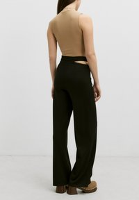 Tan geribbelde mouwloze top gecombineerd met hoge zwarte wijde broek met uitsnijding. Model draagt bruin chunky hakken.
