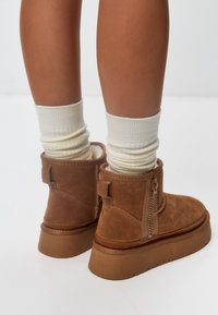 Braune Wildleder-Ankle-Boots mit einem seitlichen Reißverschluss, strukturiertem Finish und einer dicken Plattformsohle. Kombiniert mit cremefarbenen gerippten Socken.