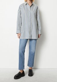 Button-up shirt with thin blue and white stripes; long sleeves with striped cuffs. Paired with light blue straight-leg jeans and black loafers.