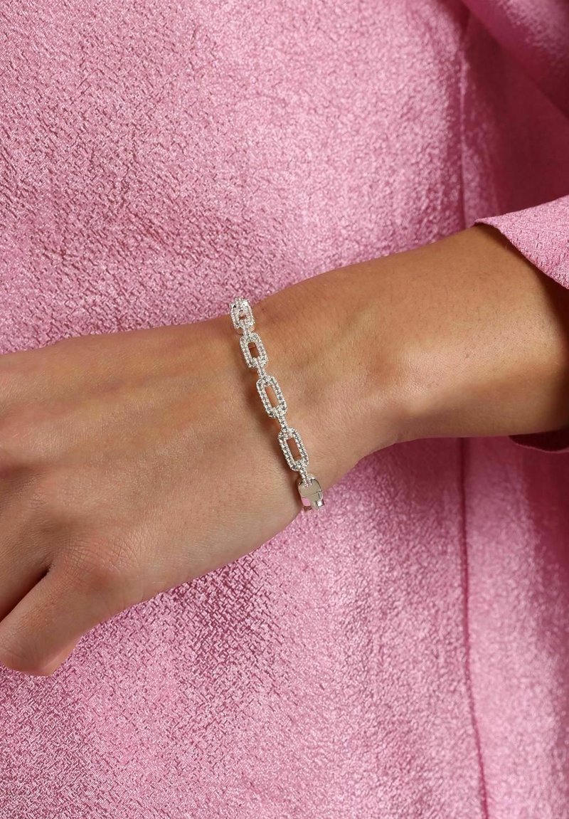 Silver kedja armband med rektangulära länkar, med en glittrande yta. Mot en strukturerad rosa bakgrund.