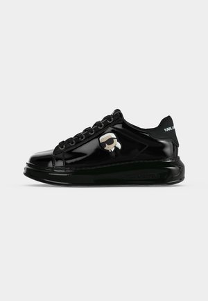 Sort blank sneaker med tyk sål, sorte snørebånd, tegneserie-logo på siden og hvid tekst "KARL LAGERFELD" på hælflappen.