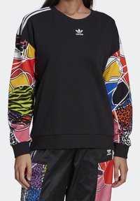 Zwarte sweatshirt met kleurrijke gebloemde mouwen met dierenprints en abstracte ontwerpen. Adidas-logo op de borst, geribbelde manchetten en zoom.