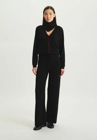 Ensemble noir en deux pièces comprenant un haut à manches longues avec un décolleté en V et des accents rouges, associé à un pantalon large, fabriqué en tissu doux.