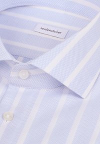 Chemise rayée bleu clair et blanc avec des boutons blancs et une étiquette "seidensticker" à l'intérieur du col.