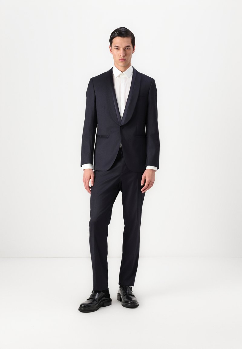 Námornícky oblek s jedným gombíkom, klopovými goliermi a slim fit nohavicami. Skombinovaný s bielou košeľou a čiernymi spoločenskými topánkami.