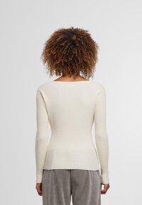 Rippstrickoberteil in Off-White, mit langen Ärmeln und weitem Ausschnitt. Der Stoff hat eine weiche Textur, mit einer figurbetonten Silhouette und Seiten-Schlitzen.