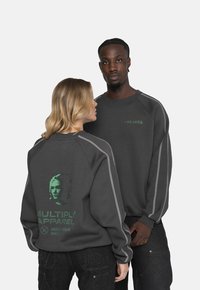 Sudadera gris con un estampado gráfico verde de una cara y texto en la parte posterior, con costuras grises contrastantes a lo largo de los hombros.