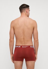 Boxeri din nailon roșu cu un tiv alb cu logo-ul Nike, având o potrivire strânsă și o textură netedă. Designul este simplu și modern.