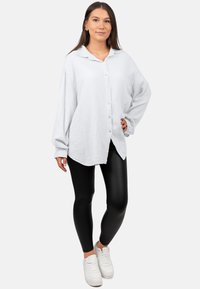Witte, gestructureerde overhemd met kraag, lange mouwen en een afgeronde zoom, gecombineerd met zwarte leggings en witte sneakers.