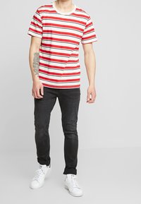 Camiseta de rayas rojas y blancas con mangas cortas y escote redondo, combinada con jeans negros y zapatillas blancas.