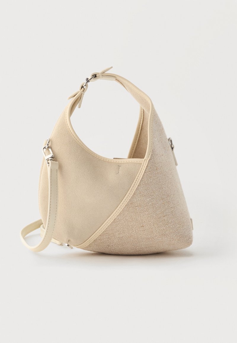 Sac à main beige en forme de croissant avec textures de tissus mélangées, poignée courte et bandoulière amovible, sur fond clair.