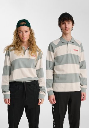 Long-sleeve polo shirts in light beige and green stripes. Each features a collar and red logo. Model pairs with black pants, one wears a cap.