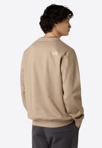 Beige crewneck sweatshirt lavet af blødt stof, med et lille hvidt logo på ryggen. Casual pasform med ribstrikkede manchetter og kantdetaljer.