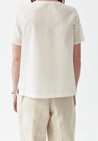 Haut en lin blanc à manches courtes avec un col rond et des fentes sur les côtés. Associé à un pantalon en lin beige clair. Apparence simple et texturée.