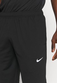 Zwarte sportbroek van lichtgewicht stof, met een elastische tailleband en een wit Nike-logo op de linkerdij.