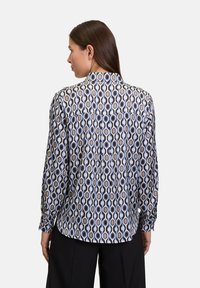 Camicia a maniche lunghe in tessuto leggero, caratterizzata da un motivo geometrico di forme a goccia blu e beige, con una schiena con bottoni e colletto.