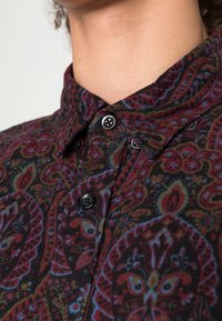 Button-up shirt featuring a black fabric with intricate paisley patterns in red, green, and blue, complemented by black buttons.