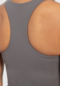Top deportivo gris con diseño de espalda nadadora. Fabricado con un material suave que presenta una textura sutil y un logo en la parte inferior.