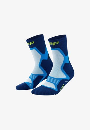 Ein Paar blaue Sportsocken mit hellblauen geometrischen Mustern und gelben Logo-Akzenten, halblang, vor einem weißen Hintergrund präsentiert.