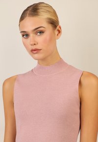 Ärmelloses Top mit hohem Kragen aus leicht rosa Rippstrick. Glatte Textur mit einer figurschmeichelnden Silhouette. Subtiler Glanz verleiht dem Stoff Dimension.