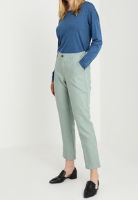 Haut à manches longues bleu clair associé à un pantalon tailleur vert menthe et des mules noires. Les détails clés incluent une fermeture à bouton et une coupe slim.