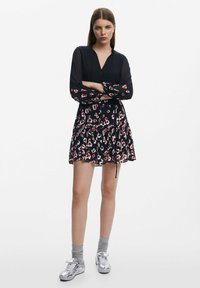 Schwarzes Kleid mit rot-weißen Blumenmuster, Knopfleiste am Ausschnitt, lange Ärmel, tailliert, schichtiger Rock, kombiniert mit silbernen Sneakers.