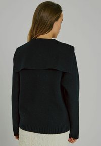 Schwarzer Strickpullover mit einem breiten, strukturierten Kragen, gerippten Bündchen und Saum. Die Textur wirkt weich; das Design hat eine lockere Passform.