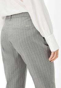 Grijze broek met streepjes in een slim fit, met een achterzak en gestikte details. Gemaakt van een gebreide stof, aangevuld met een witte blouse.