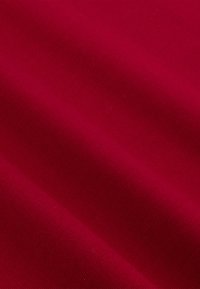 Rode katoenstof met een gladde textuur, met een effen kleur en een lichte glans, gedrapeerd om plooien en diepte te tonen.
