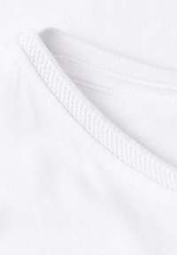 Gros plan d'un col en tissu blanc avec bordure côtelée texturée et détails de couture visibles sur un matériau en coton lisse.