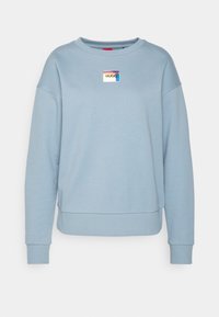 Felpa azzurra con collo rotondo e maniche lunghe, dotata di un piccolo patch rettangolare lucido con il logo "HUGO" centrato sul petto.
