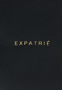Black leather surface with embossed text "EXPATRIÉ" in gold. Text is centered and features a modern, sans-serif font.