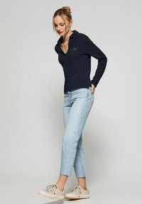 Polo de manga larga azul marino con cuello; combinado con jeans cortos azul claro y zapatillas color crema. Diseño simple y casual.