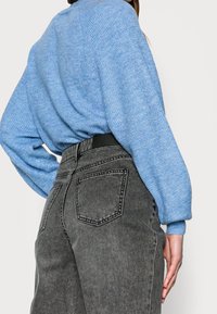 Suéter de punto azul claro con patrón texturizado, combinado con pantalones de mezclilla de talle alto en gris oscuro con costuras en contraste y detalles en los bolsillos.