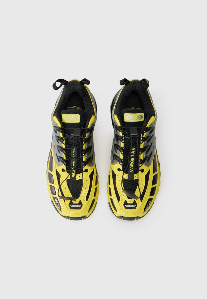 Et par gule og sorte Salomon sneakers med hurtigsnørringssystem, set ovenfra på en hvid baggrund.