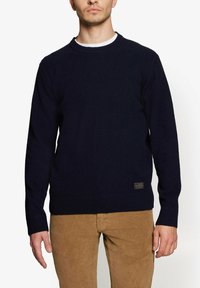 Marineblå striktrøje med rund hals, ribbede manchetter og kant, med et lille mærkelabel på den nederste venstre side.