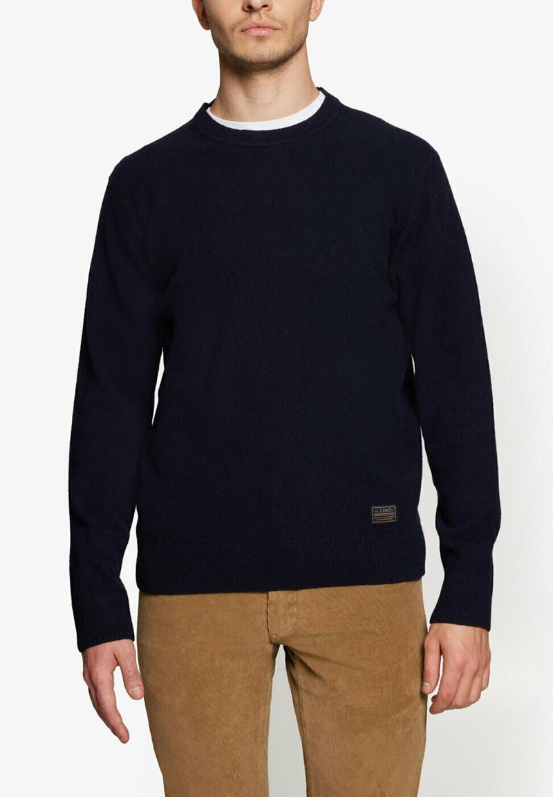 Marineblå striktrøje med rund hals, ribbede manchetter og kant, med et lille mærkelabel på den nederste venstre side.