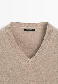 Maglione beige a scollo a V realizzato in morbido tessuto a maglia. Presenta collo e orlo a coste con una texture sottile. L'etichetta interna reca la scritta "Massimo Dutti".