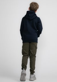 Navy hoodie met een trekkoord en grote achterzak, gecombineerd met olijfgroene cargobroek met zijzakken, gedragen met grijze sneakers.