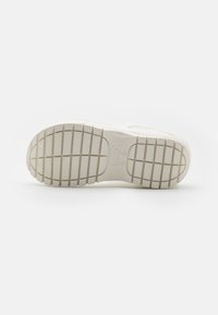 Semelle de sneaker blanche avec un motif texturé, comportant de profonds sillons pour l'adhérence. Le matériau en caoutchouc a une finition lisse et un branding subtil.