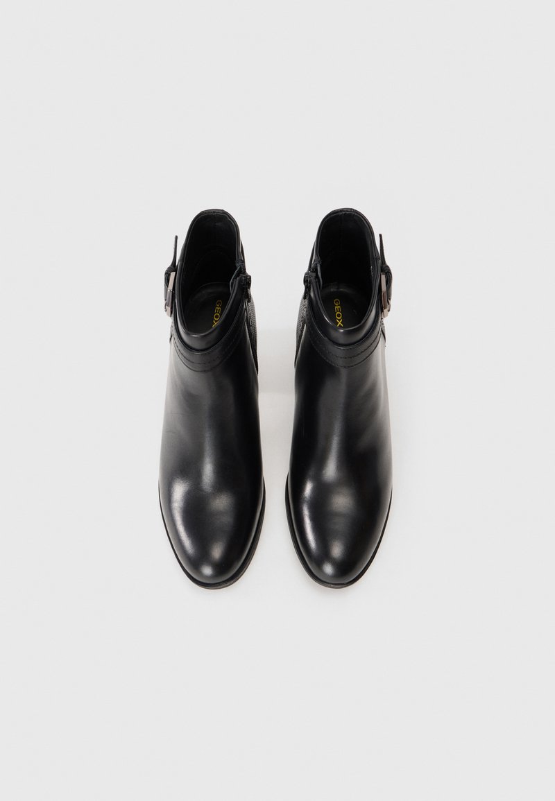 Bottines en cuir noir avec un design à bout pointu, fermeture éclair et une sangle décorative sur le côté. Texture lisse avec un minimum de détails.